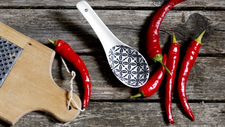 Rote Chilis liegen auf einem rustikalen Holztisch, neben einer Kelle zum Portionieren f&uuml;r scharfe Chili-Gerichte.