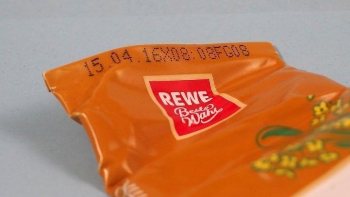 Eine ge&ouml;ffnete Tube mit dem Haltbarkeitsdatum "15.04.15" ist auf einer hellen Oberfl&auml;che platziert, das Logo von REWE ist sichtbar.