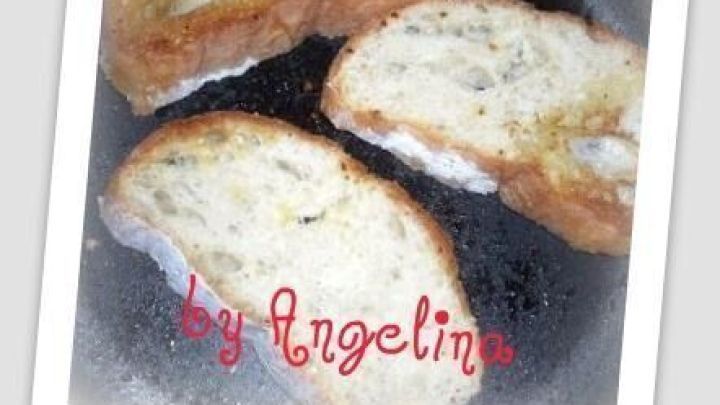 Ger&ouml;stete Ciabatta-Scheiben brutzeln in einer Pfanne, knusprig gebr&auml;unt. Text: "by Angelina" in roten Buchstaben.