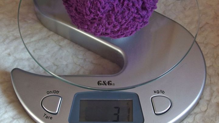 Ein lila Wollkn&auml;uel liegt auf einer digitalen Waage, die 37 Gramm anzeigt, auf einem hellen, weichen Untergrund.