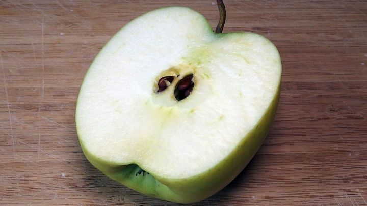 Ein geschnittenem gr&uuml;ner Apfel liegt auf einem Holzbrett und zeigt seine frische, saftige Innenseite mit Kernen.