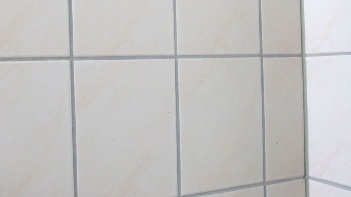 Helle Fliesen mit grauen Fugen, die Schimmelflecken aufweisen, in einem Badezimmerstil, der Sauberkeit erfordert.