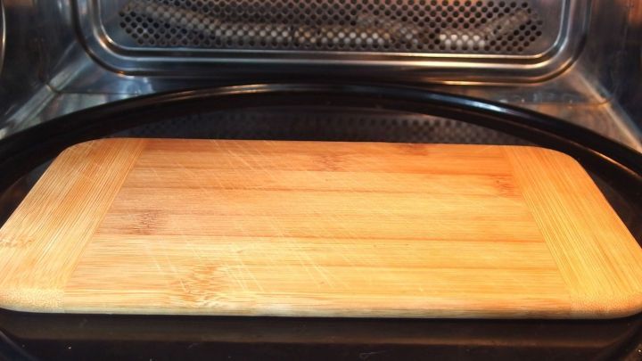 Ein Holzschneidebrett liegt in der Mikrowelle, bereit zur Reinigung durch Erw&auml;rmung in einem sauberen, neutralen Umfeld.