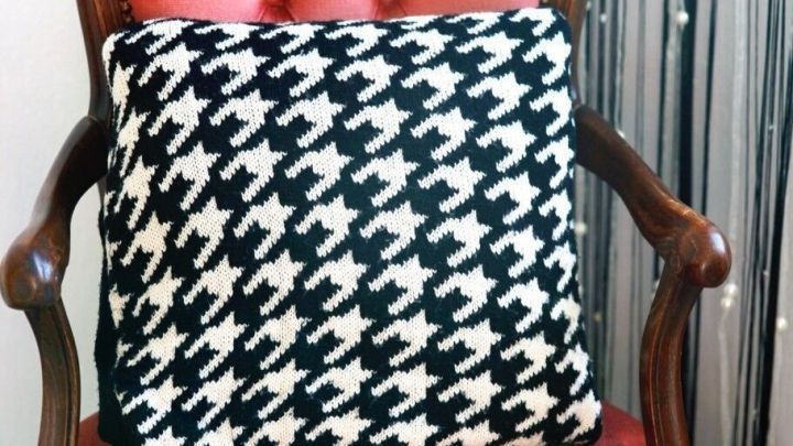 Ein Kissen aus einem alten Pullover liegt auf einem roten, gepolsterten Stuhl vor einem dekorativen, glitzernden Hintergrund.