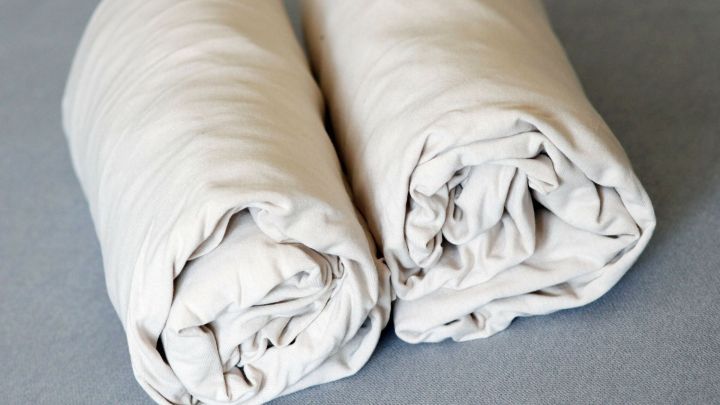 Zwei ordentlich gerollte Spannbettlaken liegen auf einem grauen Untergrund, bereit zum Verstauen oder Transport.