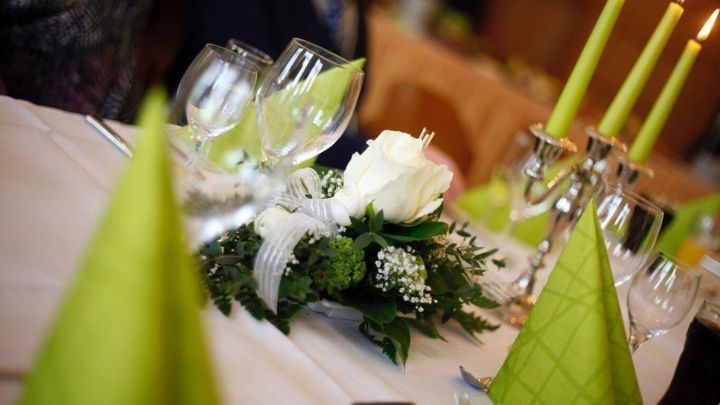 Ein eleganter Tisch ist liebevoll gedeckt mit Gl&auml;sern, einer Blumenmitte und leuchtend gr&uuml;nen Servietten.