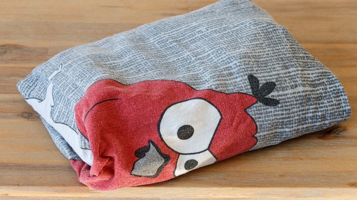 Eine gefaltete Bettw&auml;sche mit einem roten Angry Birds-Motiv liegt ordentlich auf einem Holztisch, bereit zur Aufbewahrung.