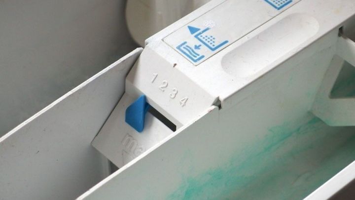 Ein Waschmittelschacht in einer Waschmaschine zeigt R&uuml;ckst&auml;nde, w&auml;hrend das Wasser mit Waschmittel in den unteren Bereich flie&szlig;t.