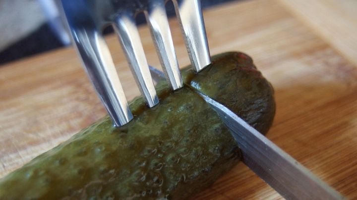 Ein Gurke wird mit einem Messer auf einem Holzbrett geschnitten, w&auml;hrend eine Gabel sie fixiert.