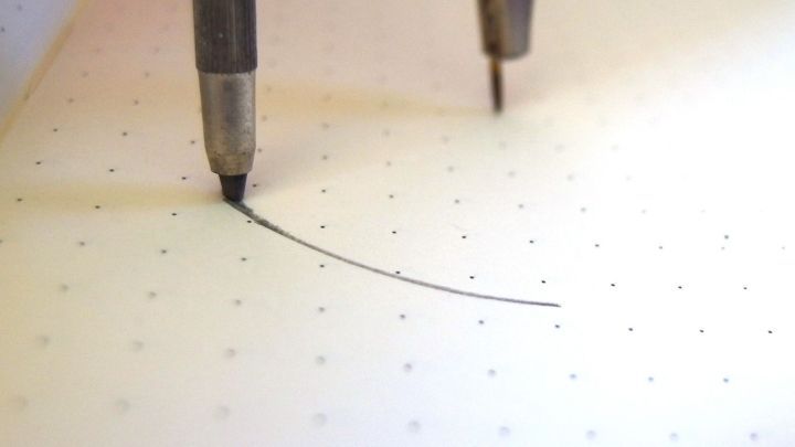 Ein Zirkel zeichnet eine pr&auml;zise Kurve auf kariertem Papier, w&auml;hrend er auf einer klaren Linie positioniert ist.