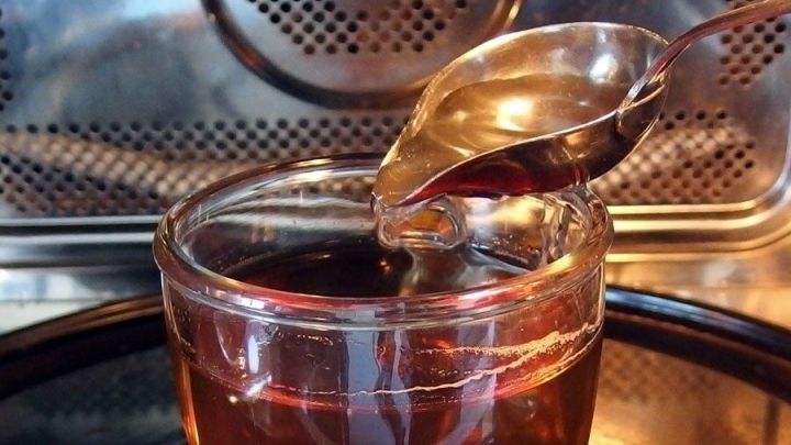 Ein Glas mit Tee wird gerade in der Mikrowelle erhitzt, w&auml;hrend ein L&ouml;ffel schr&auml;g dar&uuml;ber h&auml;ngt.