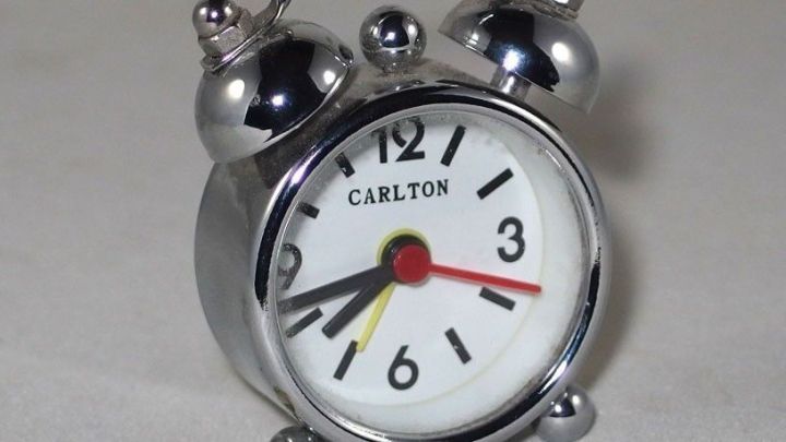 Ein klassischer Wecker steht auf einem Tisch und zeigt kurz nach sechs Uhr, bereit, den Morgen einzul&auml;uten.