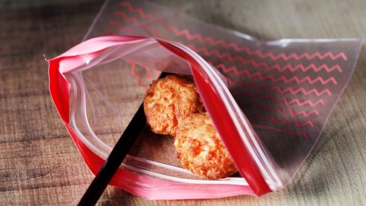 Eine durchsichtige T&uuml;te mit zwei frittierten B&auml;llchen und einem Strohhalm, bereit zum Einfrieren, auf einem Holzuntergrund.