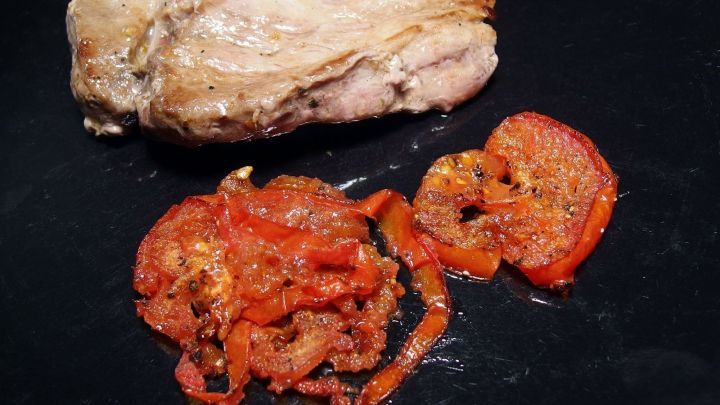 Gebratene Tomaten liegen appetitlich neben einem saftigen Steak auf einer schwarzen Platte, bereit zum Servieren.