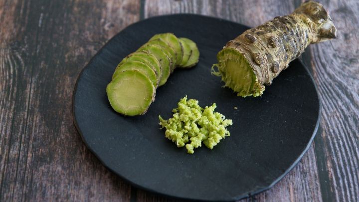Auf einem schwarzen Teller liegen frisch geschnittene Wasabi-Scheiben und eine Portion gr&uuml;ne Wasabipaste, umgeben von Holztextur.