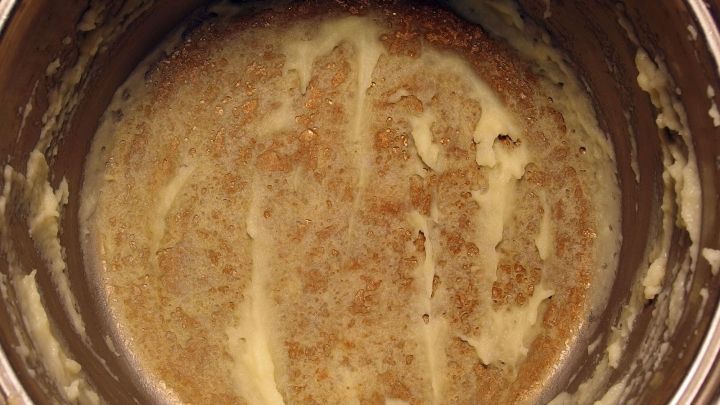 Ein metallener Topf mit angebrannten Zwiebeln darin zeigt braune R&uuml;ckst&auml;nde und Reste am Boden und den Seiten.