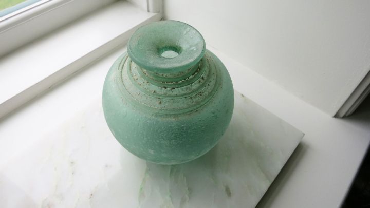 Eine gr&uuml;nliche Glasblumen vase steht auf einem wei&szlig;en Tisch in der N&auml;he eines Fensters, lichtdurchflutet und sauber.