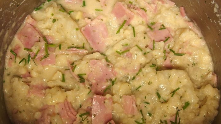 Ein cremiges Gericht aus Blumenkohl in Schinkenso&szlig;e, das in einem Topf serviert wird, umgeben von frischen Kr&auml;utern.