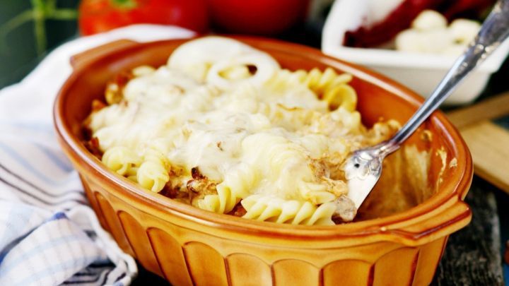 Ein gebackenes Gericht aus Nudeln mit Gyros in einer terrakottafarbenen Form, umgeben von frischen Tomaten und K&auml;se.