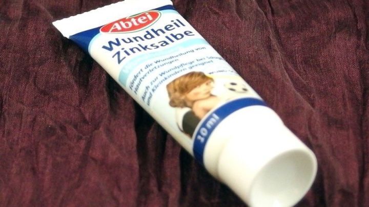 Eine zinkhaltige Salbe liegt auf einem roten Samtuntergrund, bereit zur Anwendung auf schmerzenden Narben.