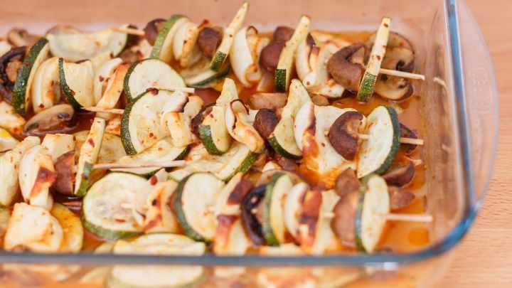 Gegrillte Halloumi-Spie&szlig;e mit Zucchini und Champignons sind in einer Auflaufform angeordnet, bereit zum Kochen.