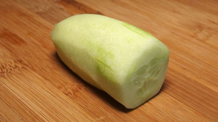 Ein gesch&auml;lter, gr&uuml;ner Gurke liegt auf einem Holzbrett, bereit zur Verwendung zur Linderung von Migr&auml;ne.