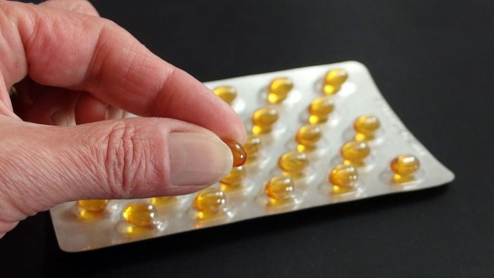 Eine Hand greift nach einer Fisch&ouml;lkapsel auf einer Verpackung, um die Fingern&auml;gel zu st&auml;rken und spr&ouml;de N&auml;gel zu behandeln.