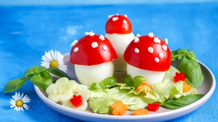 Bunte, essbare Pilze aus Eiern und Tomaten liegen auf einem Teller umgeben von frischem Salat und Kr&auml;utern.