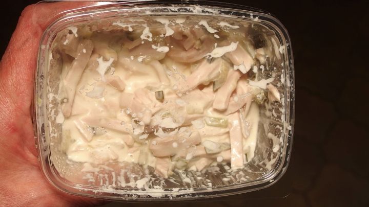 Eine Hand h&auml;lt einen durchsichtigen Beh&auml;lter mit einem schimmligen, unappetitlichen Inhalt, der unangenehme Ger&uuml;che im K&uuml;hlschrank verursachen kann.