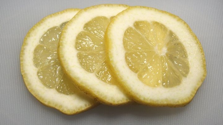 Drei frische, in Scheiben geschnittene Zitronen liegen auf einer wei&szlig;en Arbeitsfl&auml;che, bereit f&uuml;r die Verwendung gegen H&uuml;hneraugen.