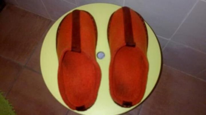 Orange Filzpantoffeln liegen auf einem kleinen, runden, gelben Tisch vor einem gefliesten Hintergrund auf dem Boden.