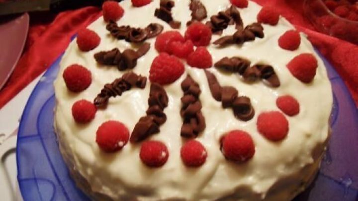 Eine Schoko-Himbeer-Torte liegt auf einem blauen Teller, dekoriert mit roten Himbeeren und Schokoladensauce in einem festlichen Raum.