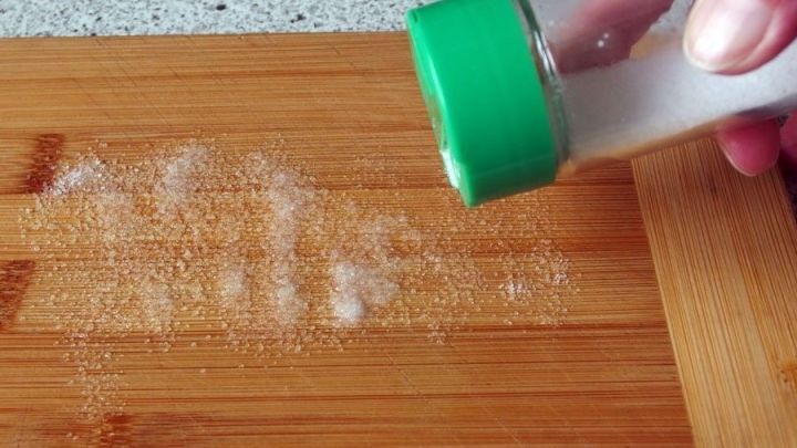 Ein Hand registriert ein Schneidbrett aus Holz, w&auml;hrend Salz dar&uuml;ber gestreut wird, um Ger&uuml;che zu neutralisieren.