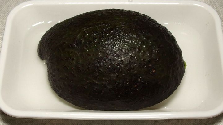 Eine gesamte Avocado liegt in einer wei&szlig;en Schale. Sie sieht frisch aus und wird zur Aufbewahrung vorbereitet.