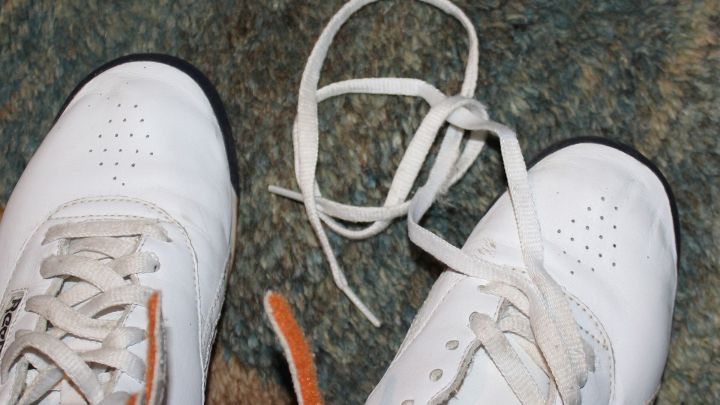 Wei&szlig;e Schuhb&auml;nder liegen ungekn&uuml;pft vor hellbeigen Schuhen auf einem gr&uuml;nlichen Teppichboden, bereit zum F&auml;rben.