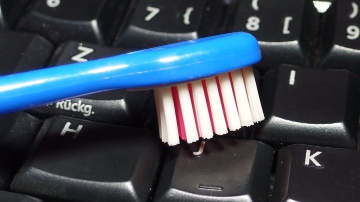 Eine blaue Zahnb&uuml;rste reinigt einige Tasten einer PC-Tastatur, um Schmutz zu entfernen und die Hygiene zu verbessern.