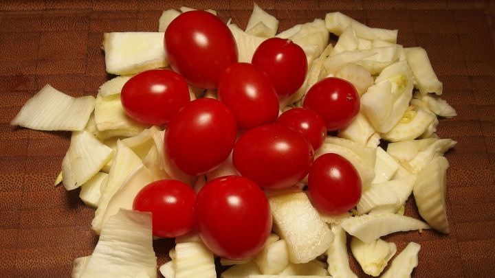 Frische, rote Kirschtomaten liegen auf einer gehackten Kohlsorte auf einem Holzbrett, bereit f&uuml;r eine gesunde Kindermahlzeit.