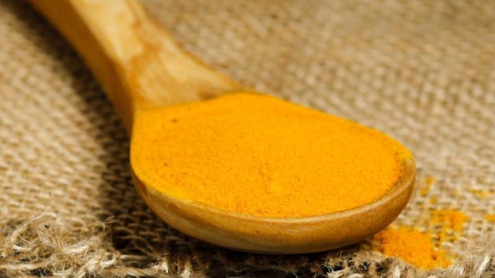 Ein L&ouml;ffel mit gelbem Curcuma-Pulver liegt auf einem groben, braunen Jutesack.