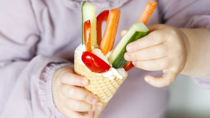 Ein Eish&ouml;rnchen voll mit buntem Gem&uuml;se wird von einem Kind gehalten, das es interessiert betrachtet und daf&uuml;r greift.