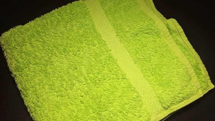 Ein gr&uuml;nes Handtuch liegt flach auf einem dunklen Untergrund, bereit, weich und angenehm in der Nutzung zu werden.