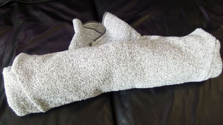 Ein zusammengerolltes Kleidungsst&uuml;ck liegt auf einer dunklen Oberfl&auml;che. Die Technik des Zusammenrollens spart Platz beim Kofferpacken.