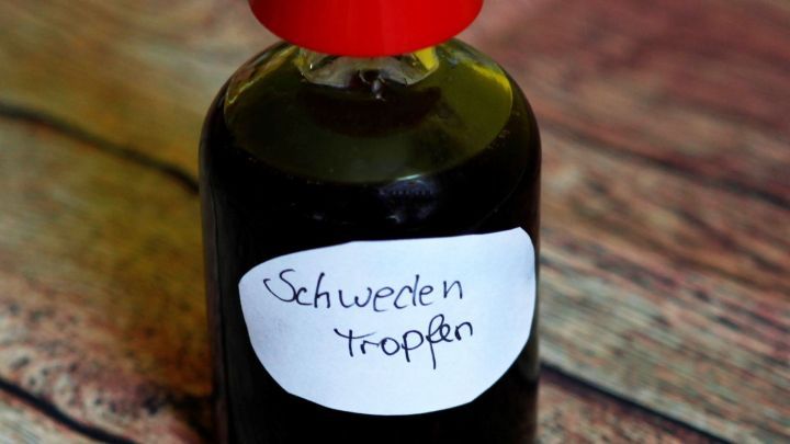 Ein Glasfl&auml;schchen mit rotem Deckel steht auf einer Holzoberfl&auml;che. Es enth&auml;lt schwarze Schwedentropfen, beschriftet.