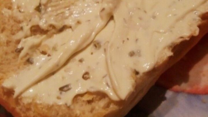 Ein Br&ouml;tchen liegt auf einem gemusterten Teller und ist mit weicher Butter bestrichen, bereit zum Verzehr.