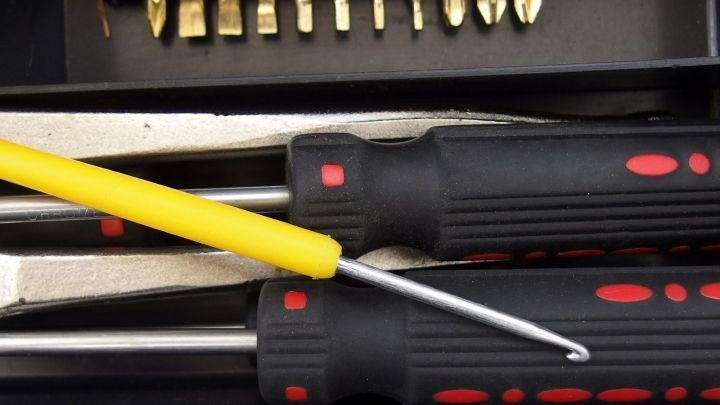 Eine H&auml;kelnadel liegt neben Schraubendrehern in einem Werkzeugkasten und k&ouml;nnte verwendet werden, um Haare aus dem Abfluss zu entfernen.