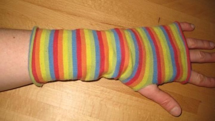 Bunte Stulpen aus alten Kniestr&uuml;mpfen liegen auf einem Holzuntergrund, w&auml;hrend eine Hand sie anzieht.