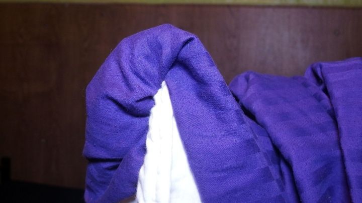 Ein lila Bettbezug wird gerade auf eine Matratze gezogen, w&auml;hrend im Hintergrund eine Holzwand zu sehen ist.