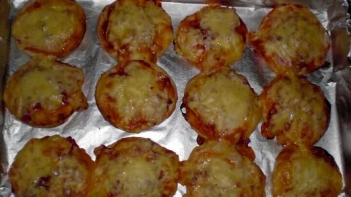 Mini-Pizzas liegen frisch gebacken auf einem mit Alufolie belegten Backblech im Ofen.