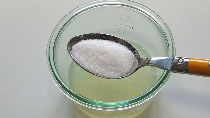 Eine L&ouml;ffel mit Zucker schwebt &uuml;ber einem Glas Zitronensaft zur Herstellung von Zitronensirup gegen Husten.