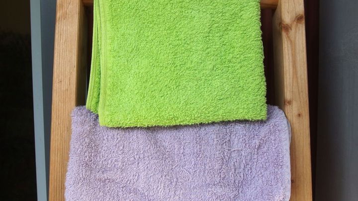 Eine Holzleiter fungiert als Handtuchhalter, auf der ein gr&uuml;nes und ein lilafarbenes Handtuch h&auml;ngen.