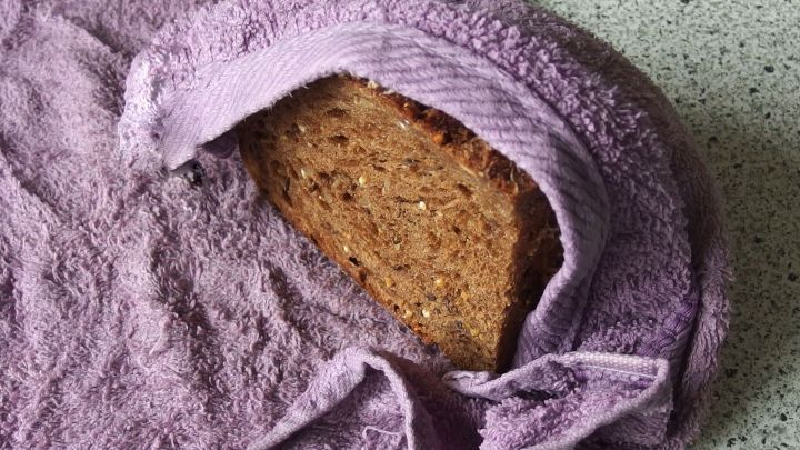 Ein St&uuml;ck altes Brot liegt teilweise eingewickelt in einem lilafarbenen Tuch auf einer grauen Arbeitsplatte.